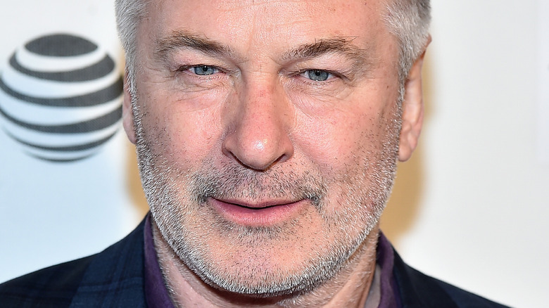 Alec Baldwin poses in a purple shirt and navy suit.