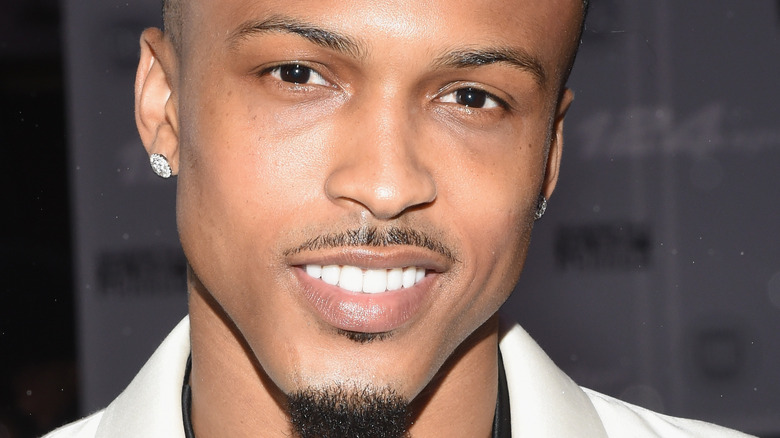 August Alsina smiles in a white suit.