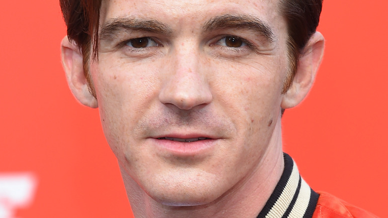 Drake Bell with serious expression in front of orange background