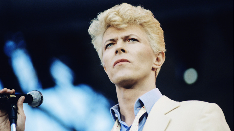 David Bowie with a microphone and blonde hair on stage in 1982