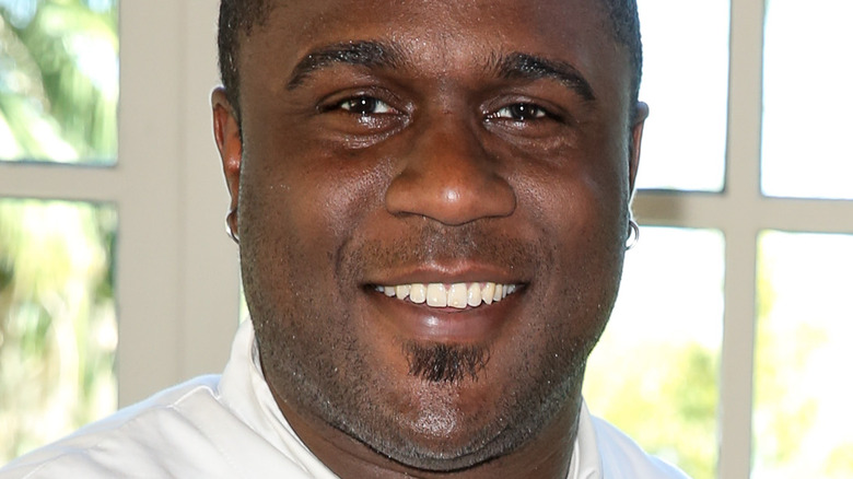 Chef Cliff Crooks, smiling, wearing a white chef's outfit, in a kitchen