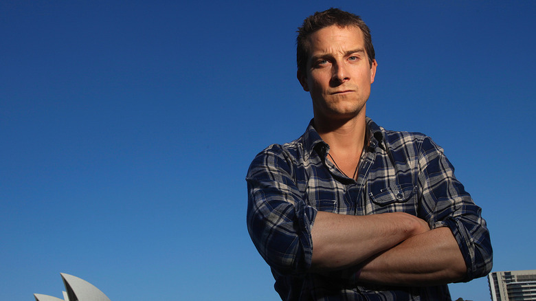 Bear Grylls in a plaid shirt, arms crossed