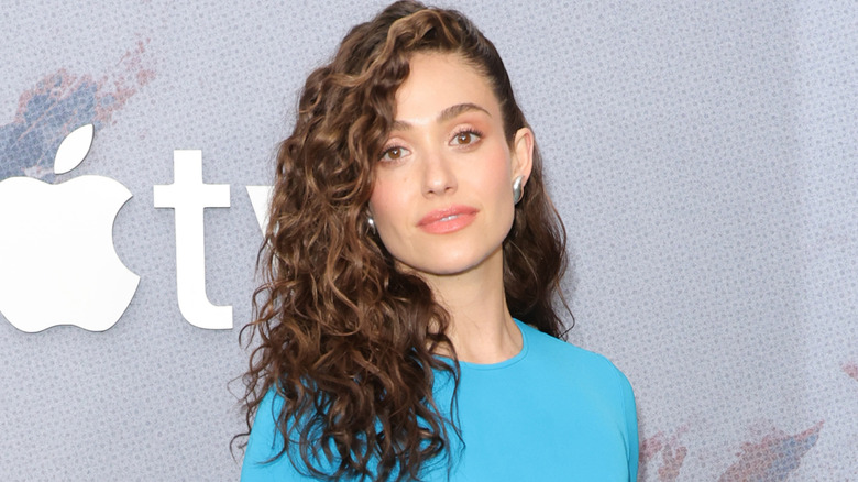 Emmy Rossum wearing a blue dress, posing in front of Apple logo