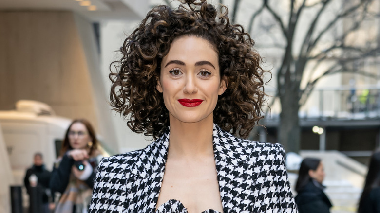 Emmy Rossum outside on a street, wearing a black-and-white checked jacket