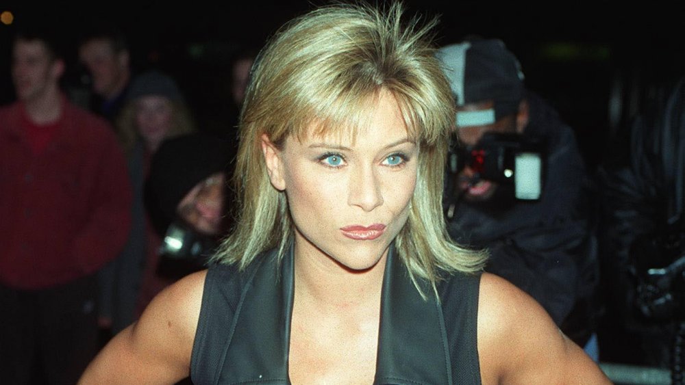 Samantha Fox in a black outfit, posing with a smirk while surrounded by photographers in the mid-90s