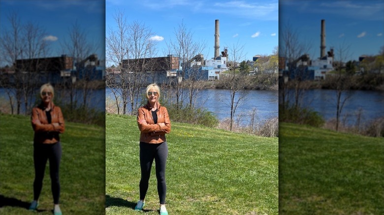 Erin Brockovich stands in front of a factory near a river