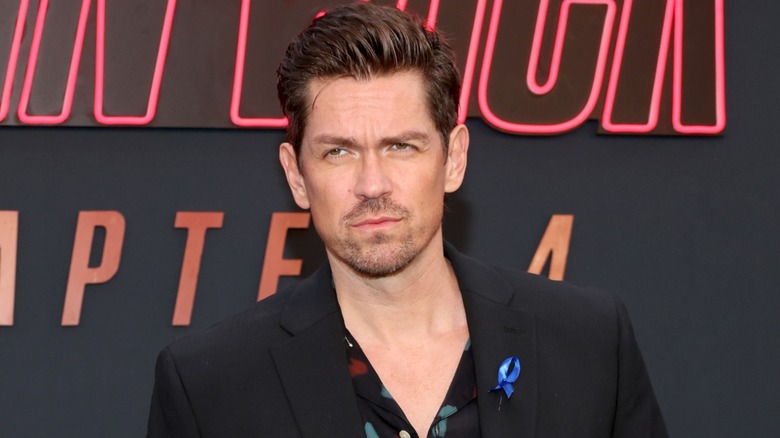 Dressed in a patterned shirt and a black suit, Steve Howey displays a cold stare.