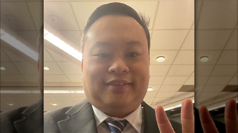 Dressed in a suit, William Hung smiles and does a peace sign