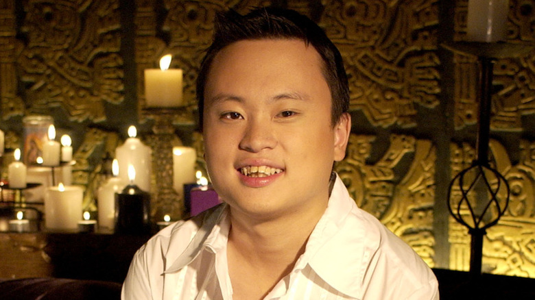 William Hung smiling in front of a music video set with lit candles