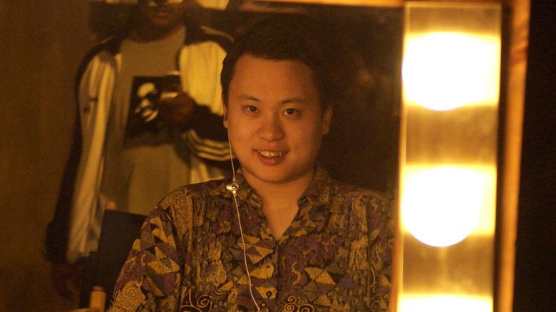 William Hung looking at himself in a vanity mirror with one ear bud in his right ear