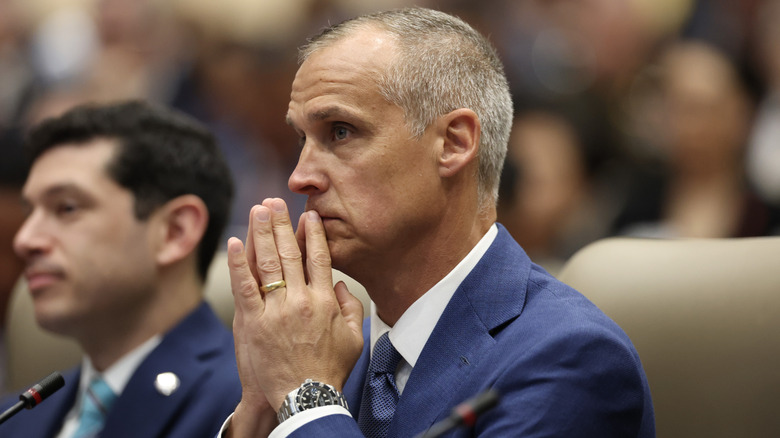 Corey Lewandowski brings his hands to his face at a conference, prominently displaying his wedding ring.