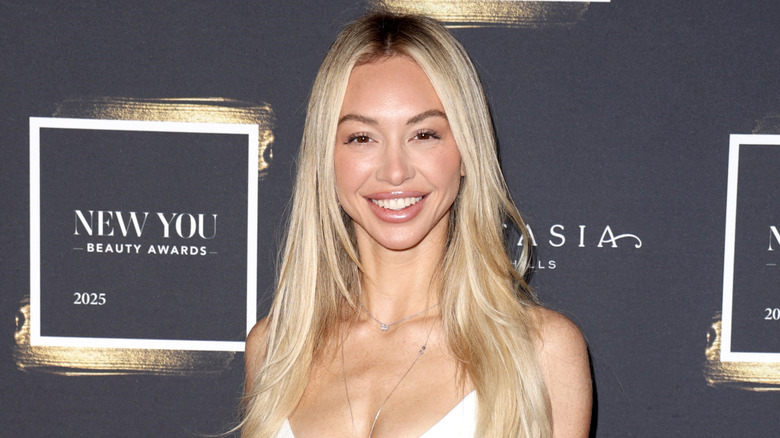 Corinne Olympios posing in front of a black-and-gold background while attending New You Beauty Awards