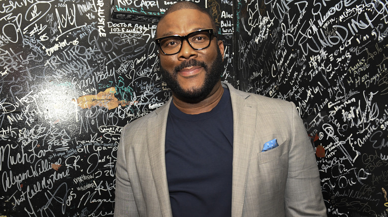 Tyler Perry smiling in front of signature-covered wall