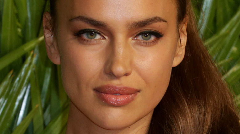 Irina Shayk poses in front of green background.