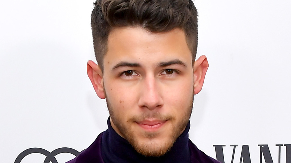 Nick Jonas looks straight ahead smiling slightly posing for cameras
