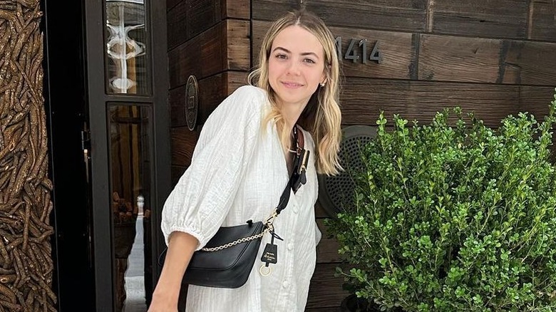 Bobbi Althoff posing in white dress and black crossbody bag