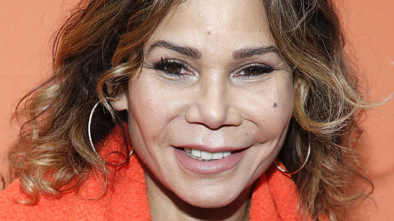 Daphne Rubin-Vega, smiling, curly hair down, against an orange background, 2020 photo