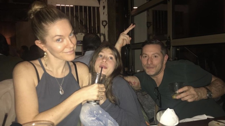 Leah McSweeney, smirking, holding her daughter Kier's drink, Rob Cristofaro, smiling, throwing up a peace sign, the three of them out to dinner
