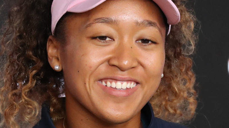 Naomi Osaka smiles while speaking to reporters