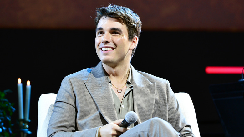 Corey Mylchreest smiles while sitting on stage an event