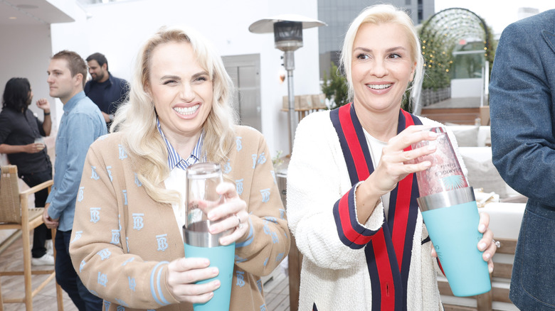 Ramona Agruma and Rebel Wilson' holding cups