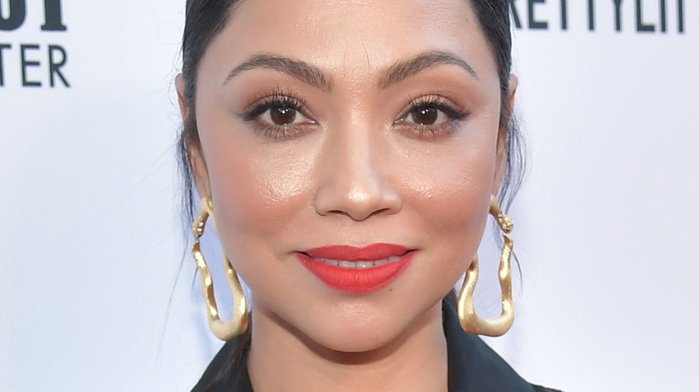 Monica Rose smiling with red lipstick and gold earrings