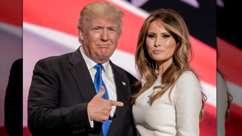 Donald Trump smirking and pointing to Melania Trump by his side