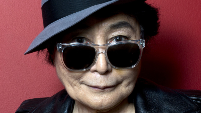 Yoko Ono poses in leather jacket, glasses and a hat.