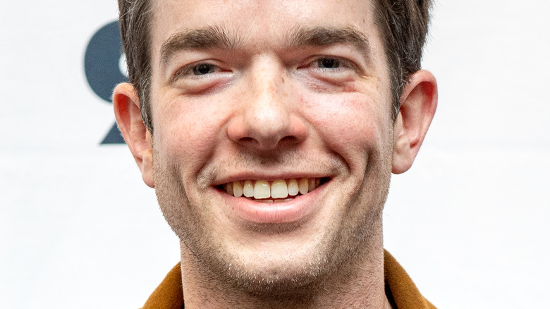 John Mulaney smiles in front of a white background