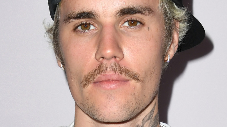 Justin Bieber, with small diamond hoop earrings and a mustache