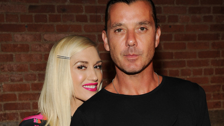 Gwen Stefani in a pink-and-black dress, smiling from behind Gavin Rossdale