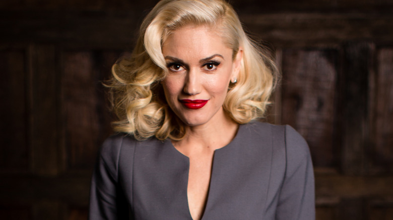 Gwen Stefani in a grey outfit and red lipstick, posing with a small smile