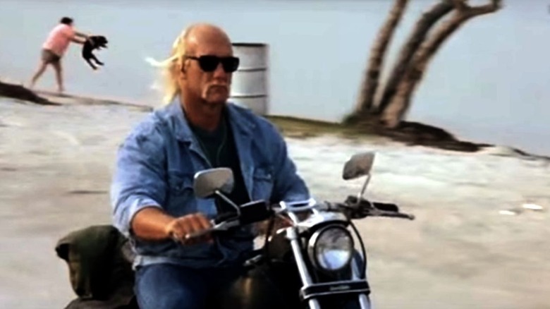 Sean Armstrong riding his motorcycle along the shore as a man throws a dog into the water in Mr. Nanny