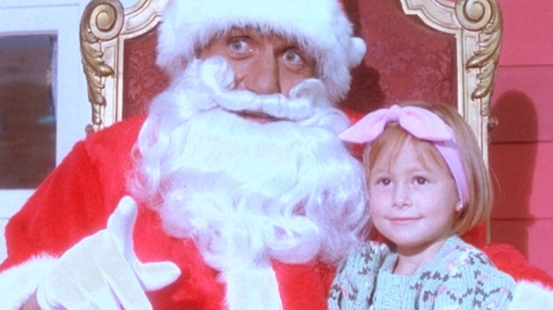Santa holding a little girl in his lap in "Santa With Muscles"
