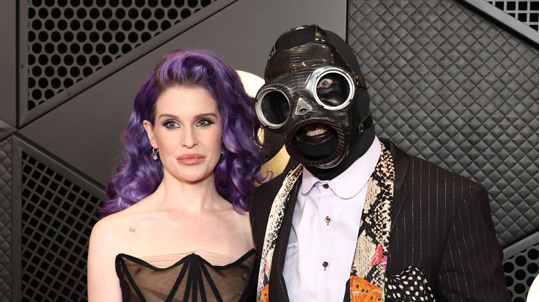 Kelly Osbourne smiles next to Sid Wilson in gas mask