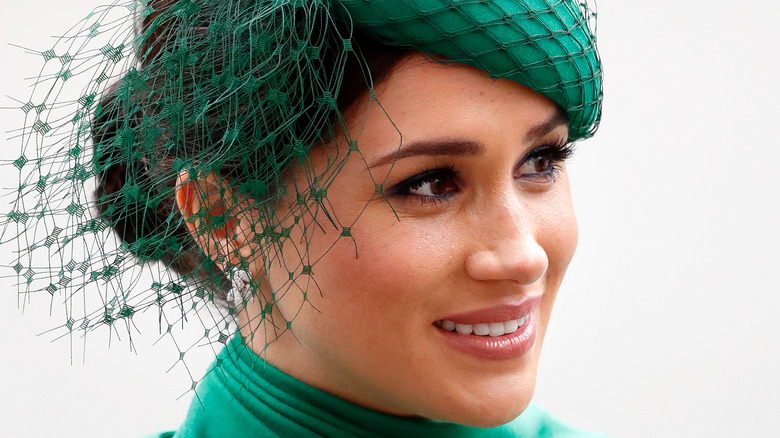 Meghan Markle smiling and looking to the side in green fascinator