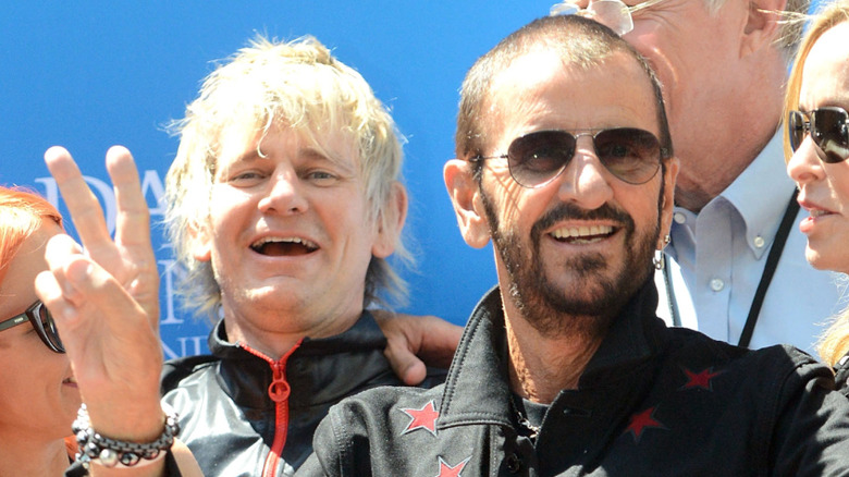 Ringo Starr flashing a peace sign in front of his son Zak Starkey.