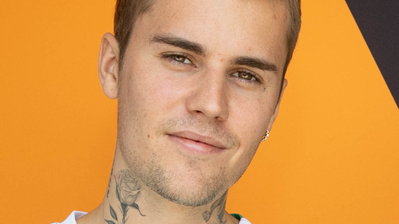 Justin Bieber poses in front of an orange backdrop.