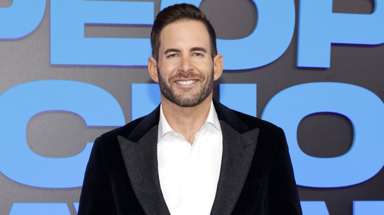 Tarek El Moussa posing in a black jacket and white suit