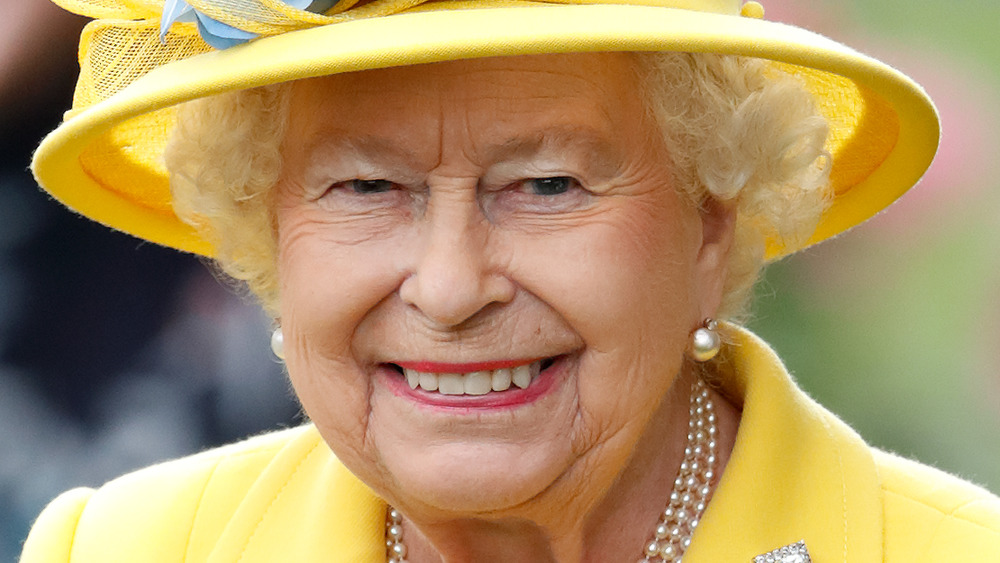 Queen Elizabeth II smiling in a yellow outfit and matching hat