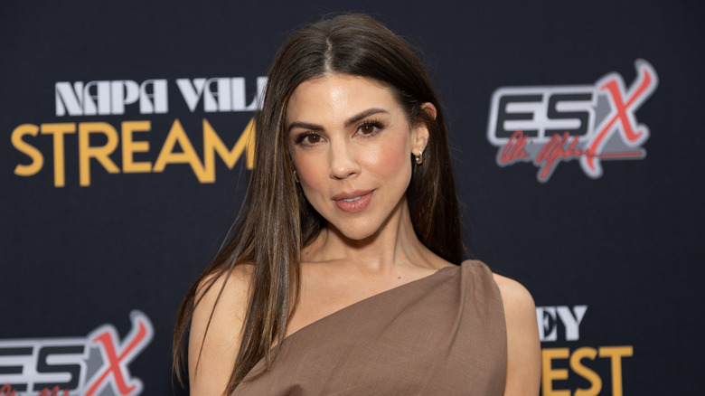 Kate Mansi posing on the red carpet in a brown one-shouldered dress