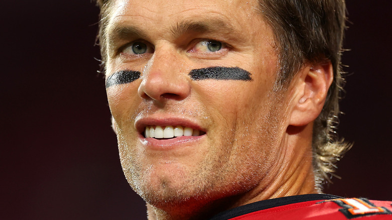 Tom Brady smiling, looking over shoulder