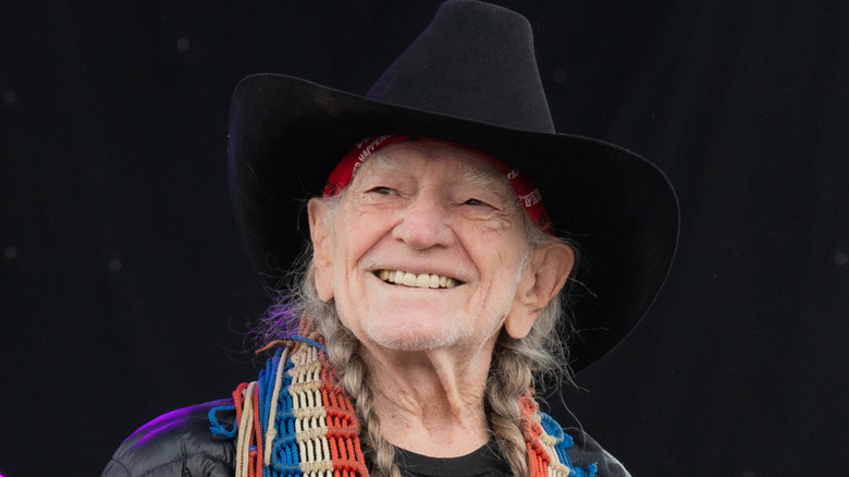 Wille Nelson smiling in a black cowboy hat on stage