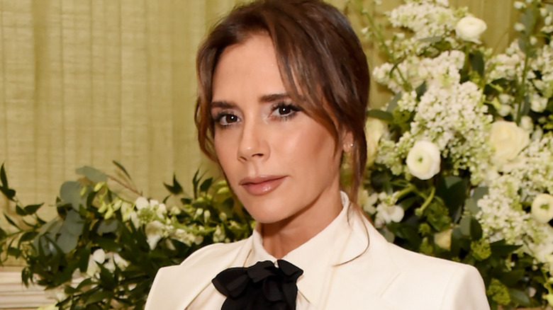 Victoria Beckham in white blazer, white blouse, and black bow