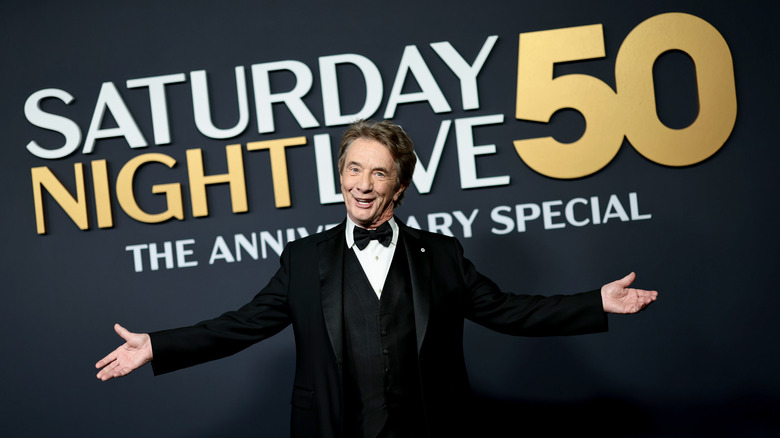 Martin Short in a tuxedo stretches his arms at the "SNL 50" red carpet