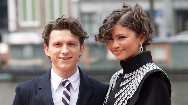 Up-close photo of Tom Holland and Zendaya smiling outdoors.
