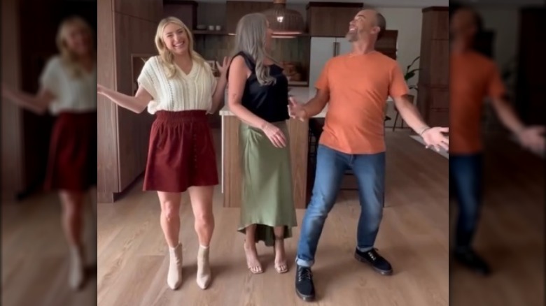 Jasmine Roth wearing a white top and maroon skirt in a kitchen with two other people.