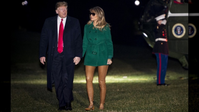 Melania Trump wearing a green jacket and tan leggings while holding hands with Donald Trump.